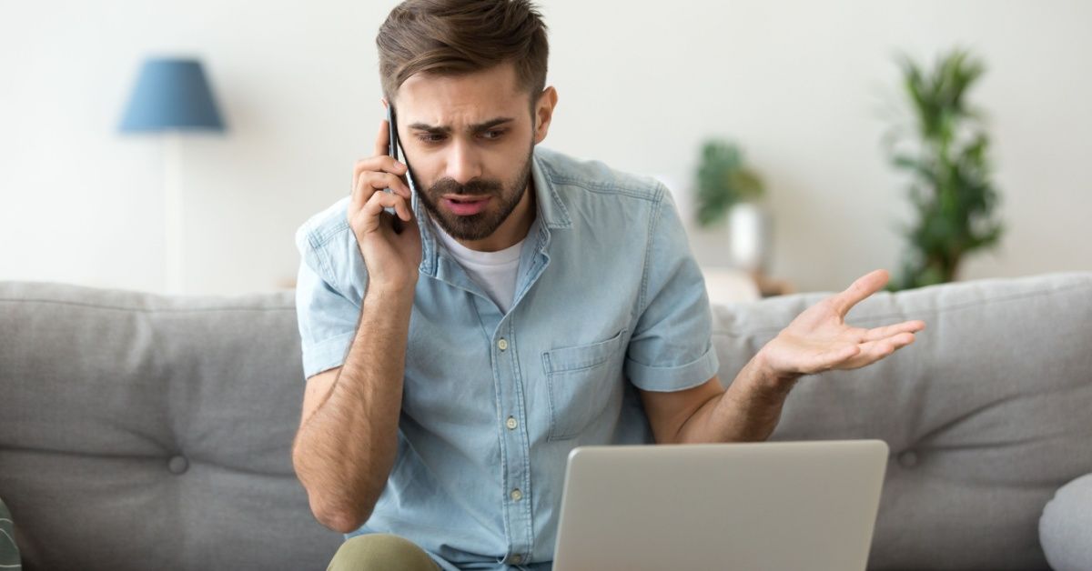 Angry man talking on phone in front of his laptop.