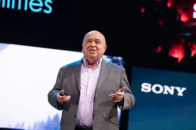 A man in a suit speaks on stage with "Sony" and other text in the background.