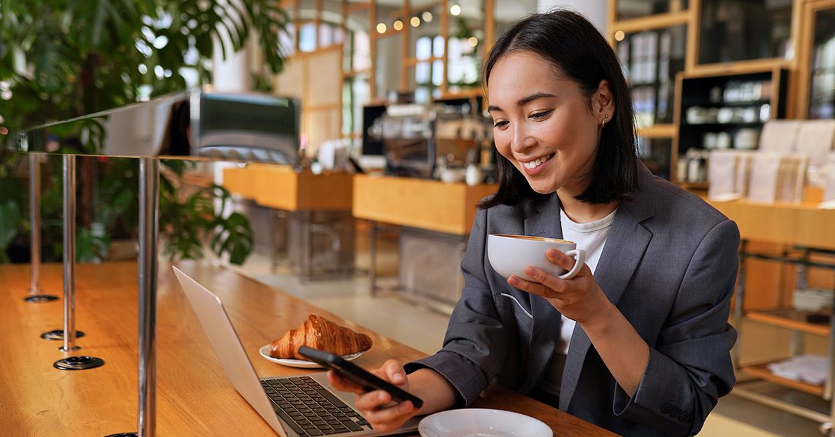 A happy young female customer using her phone and having coffee on a coffee shop.