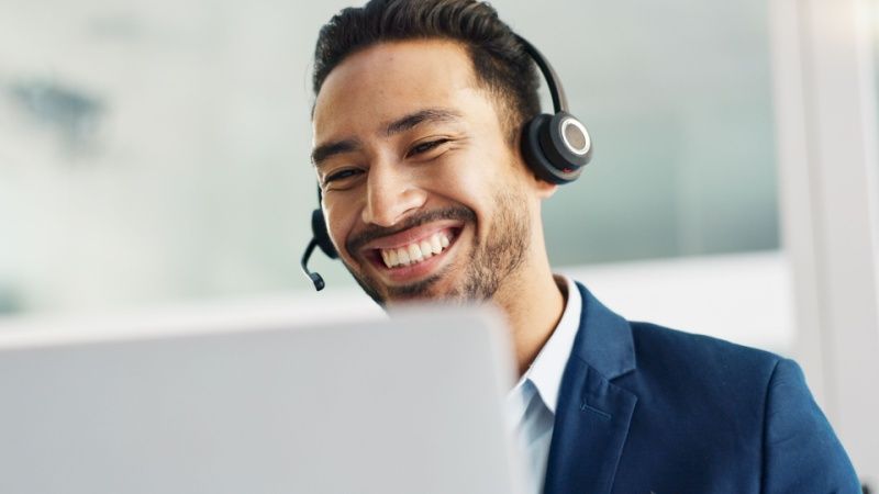 A male customer support agent smiling in front of his laptop.