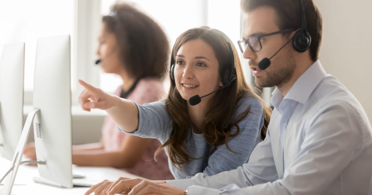 Female call center agent teaching new male agent.