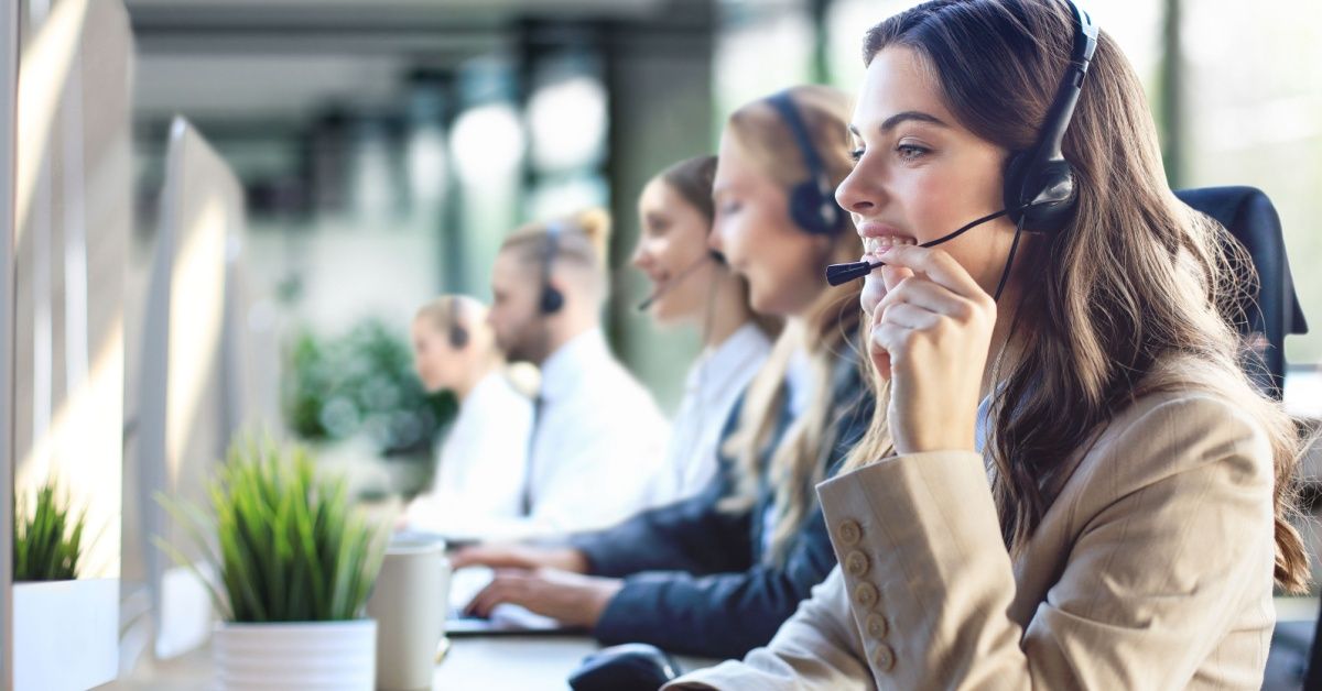 Female customer support operator with headset and smiling, with collegues at background
